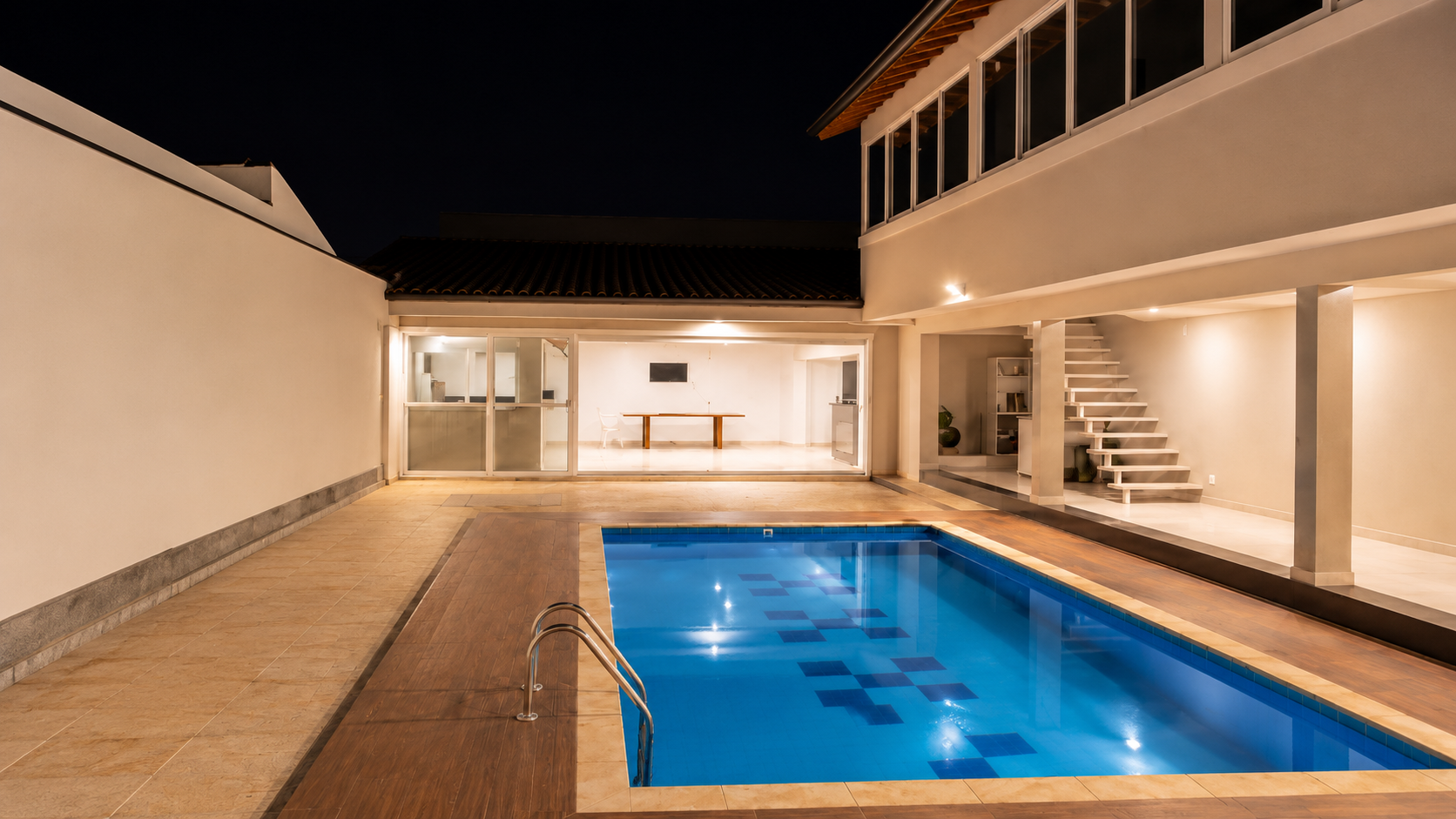 Área de lazer ao pôr do sol com churrasqueira, mesa de madeira e piscina